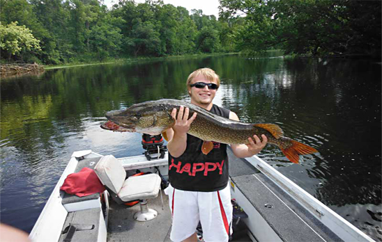 Image of young man in a boat holding up a large Northern Pike